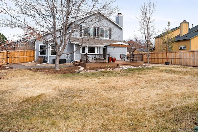 rear view of house featuring a chimney, a lawn, a wooden deck, and a fenced backyard