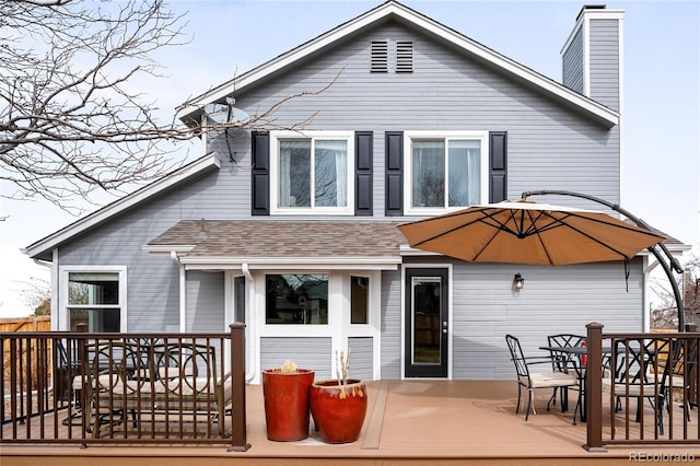 back of house featuring outdoor dining space, a deck, roof with shingles, and a chimney