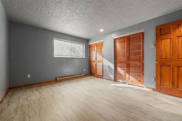 unfurnished bedroom with a textured ceiling, multiple closets, light hardwood / wood-style flooring, and a baseboard radiator