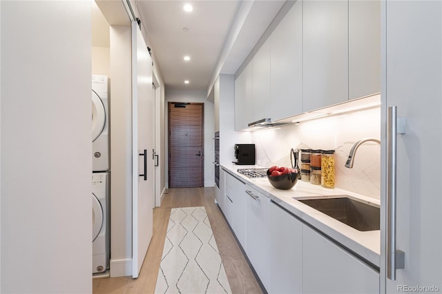 kitchen featuring sink, light hardwood / wood-style floors, white cabinets, and stacked washing maching and dryer