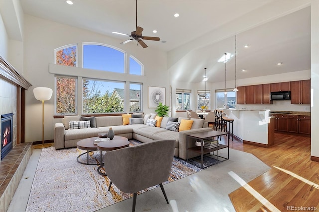 living room with ceiling fan, a fireplace, a towering ceiling, and light hardwood / wood-style flooring