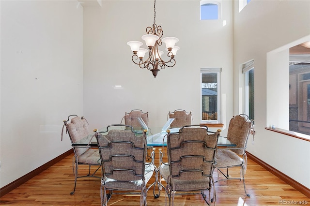 dining space with light wood-type flooring, a high ceiling, and a notable chandelier