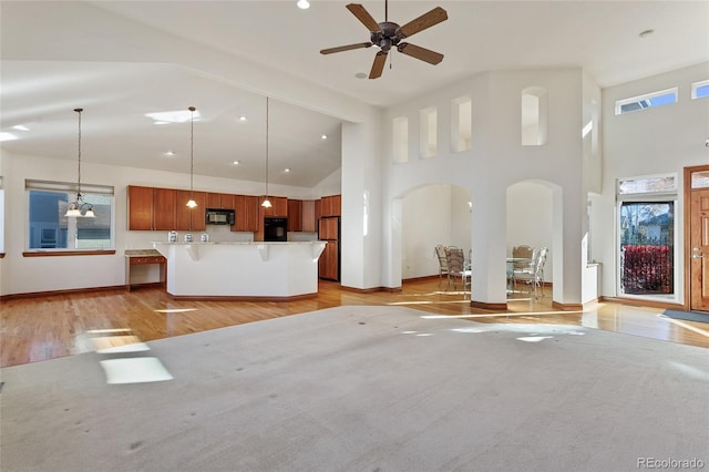 unfurnished living room featuring light wood-type flooring, ceiling fan, and a high ceiling