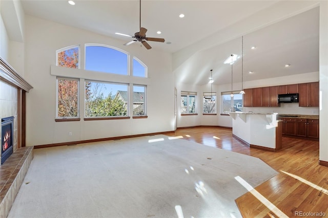 unfurnished living room with ceiling fan, a tile fireplace, and light hardwood / wood-style flooring