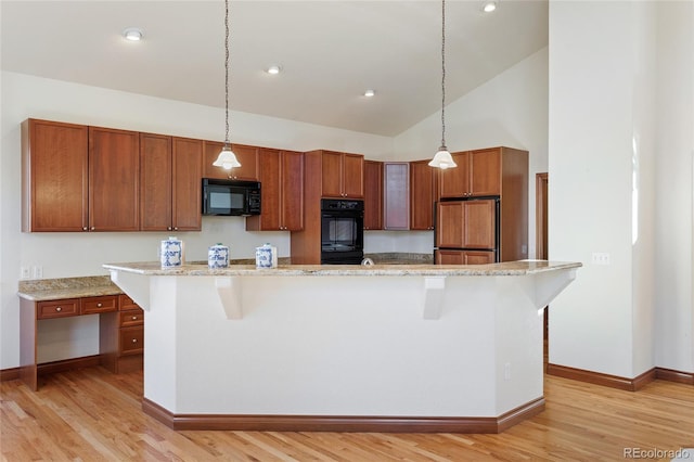 kitchen featuring black appliances, light stone countertops, hanging light fixtures, and a center island with sink