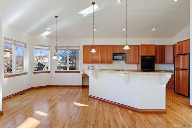 kitchen featuring an island with sink, decorative light fixtures, a kitchen breakfast bar, lofted ceiling, and black appliances