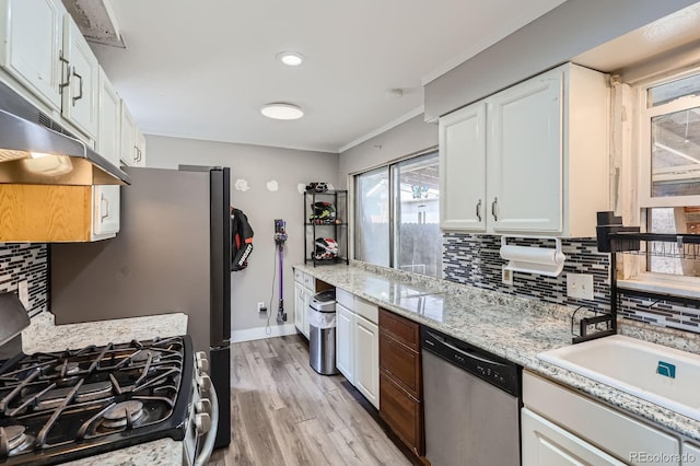 kitchen with appliances with stainless steel finishes, tasteful backsplash, white cabinets, light wood-style floors, and ornamental molding
