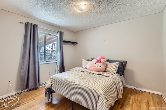 bedroom featuring wood finished floors, a textured ceiling, and baseboards
