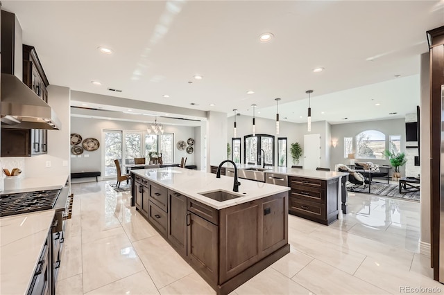 kitchen featuring pendant lighting, sink, a kitchen island with sink, dark brown cabinets, and wall chimney exhaust hood