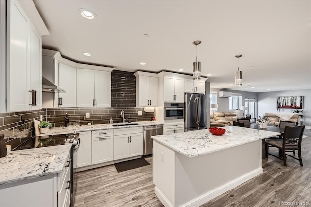 kitchen featuring a kitchen island, decorative light fixtures, sink, stainless steel appliances, and wall chimney range hood