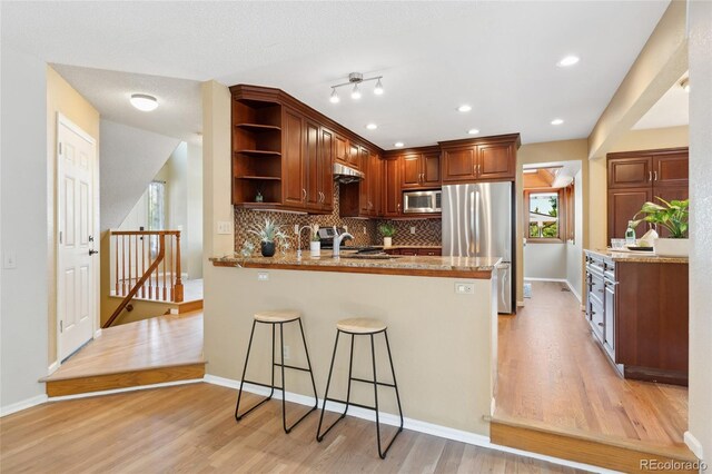 11932 W 56th Cir, Arvada, CO 80002 - kitchen with appliances with stainless steel finishes, open shelves, a peninsula, under cabinet range hood, and light wood-style floors
