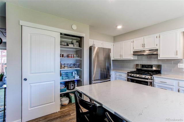 kitchen featuring dark wood-type flooring, stainless steel appliances, light stone counters, white cabinets, and decorative backsplash