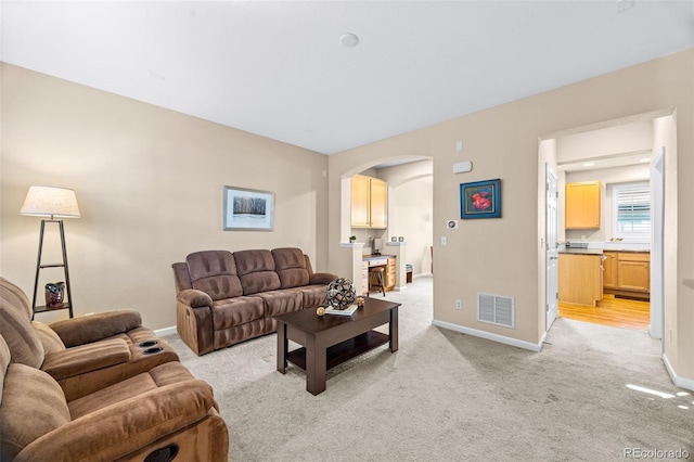 living area with light colored carpet, visible vents, arched walkways, and baseboards