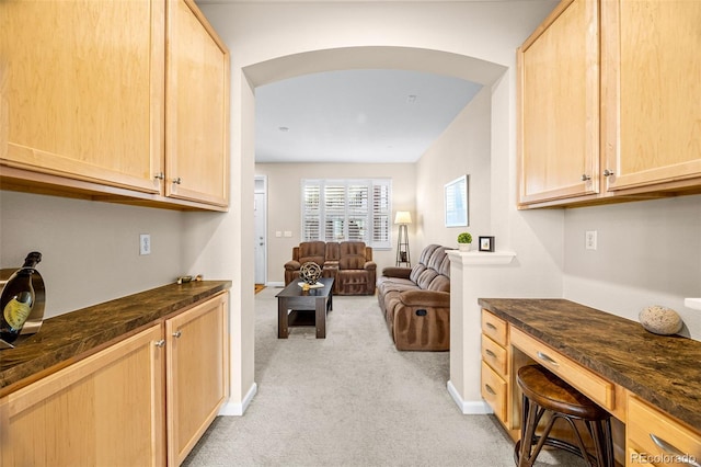 kitchen featuring dark countertops, light colored carpet, arched walkways, and light brown cabinetry