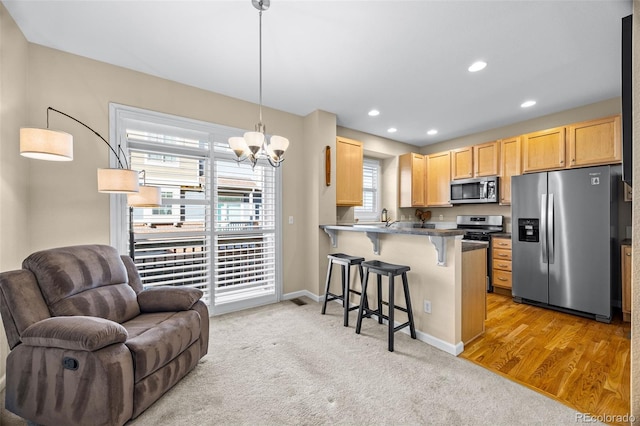 kitchen with open floor plan, a peninsula, a kitchen bar, stainless steel appliances, and light brown cabinets