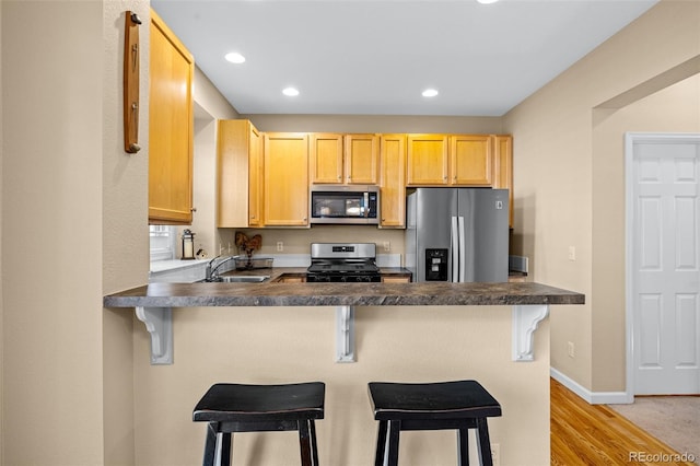 kitchen featuring dark countertops, appliances with stainless steel finishes, a sink, a peninsula, and baseboards