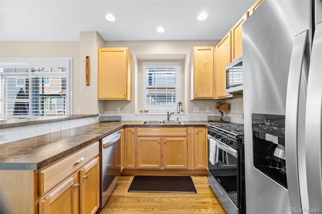 kitchen featuring stainless steel appliances, a peninsula, a sink, light wood-style floors, and dark countertops