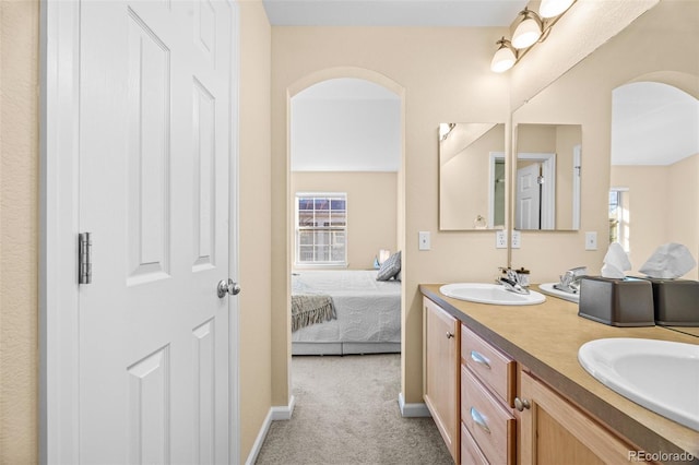 bathroom with double vanity, ensuite bath, baseboards, and a sink