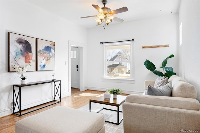 living area featuring light wood finished floors, a ceiling fan, and baseboards