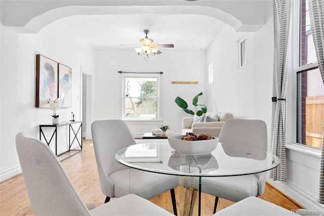 dining area with arched walkways, light wood-style floors, and ceiling fan