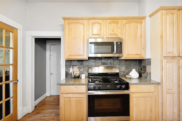 kitchen with light brown cabinets, tasteful backsplash, appliances with stainless steel finishes, and light wood-type flooring