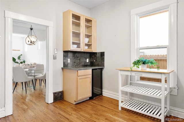 bar with wine cooler, decorative backsplash, light wood-type flooring, and baseboards