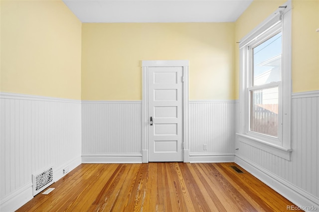 unfurnished room featuring visible vents, wainscoting, and wood finished floors