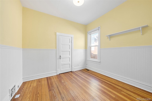 unfurnished room featuring a wainscoted wall, wood-type flooring, and visible vents