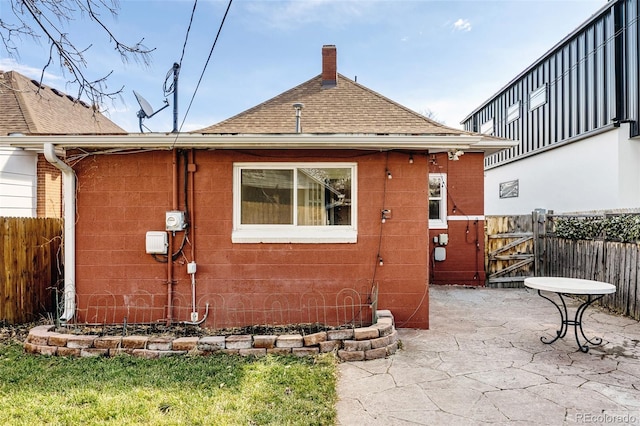 back of house with a gate, a patio, fence, roof with shingles, and a chimney