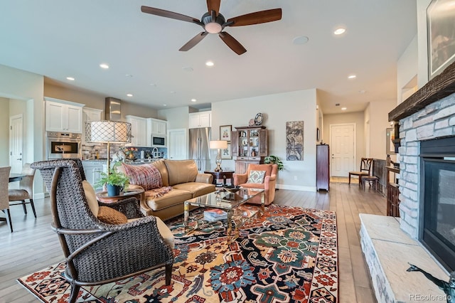 living area featuring a ceiling fan, light wood-type flooring, a fireplace, and recessed lighting