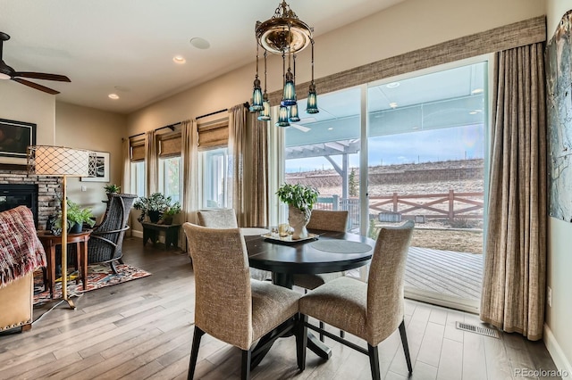 dining area featuring a ceiling fan, a fireplace, visible vents, and wood finished floors