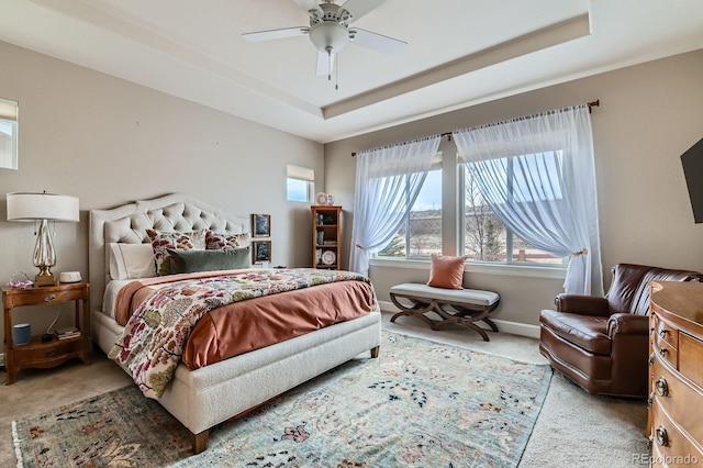 carpeted bedroom featuring ceiling fan, a tray ceiling, and baseboards