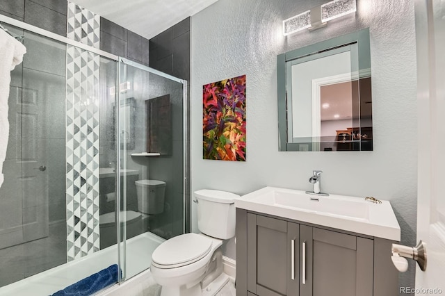 full bathroom featuring a textured wall, a shower stall, toilet, and vanity