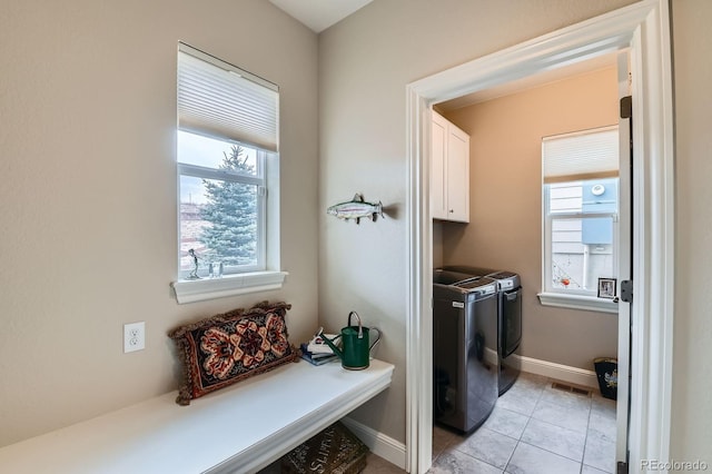 laundry area featuring light tile patterned floors, a healthy amount of sunlight, cabinet space, and washer and dryer