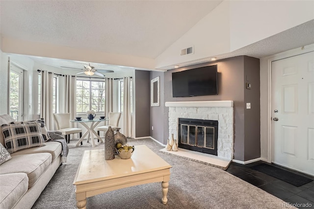 tiled living room with a ceiling fan, a stone fireplace, vaulted ceiling, baseboards, and a textured ceiling