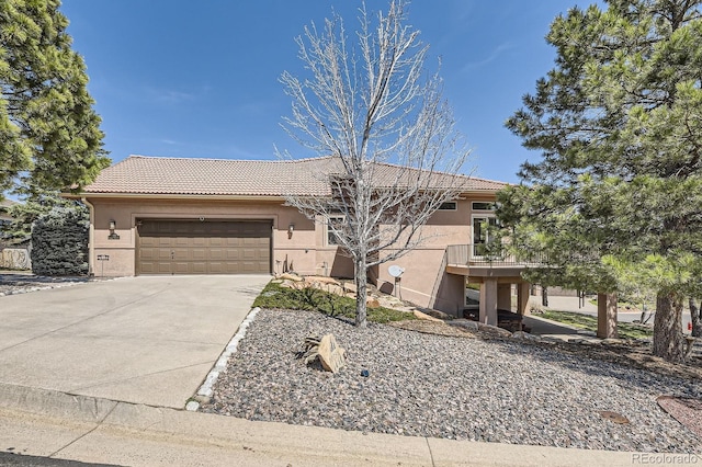 view of front facade featuring concrete driveway, a tile roof, an attached garage, and stucco siding