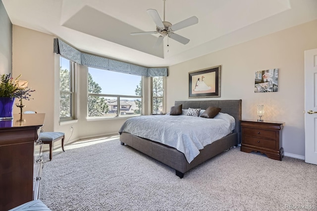 carpeted bedroom with a tray ceiling, baseboards, and ceiling fan