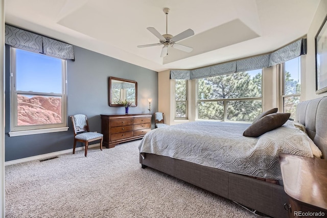 bedroom with a tray ceiling, visible vents, baseboards, ceiling fan, and carpet floors