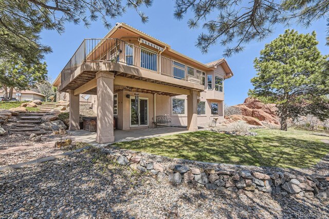 rear view of house featuring stucco siding, a patio area, a lawn, and a deck