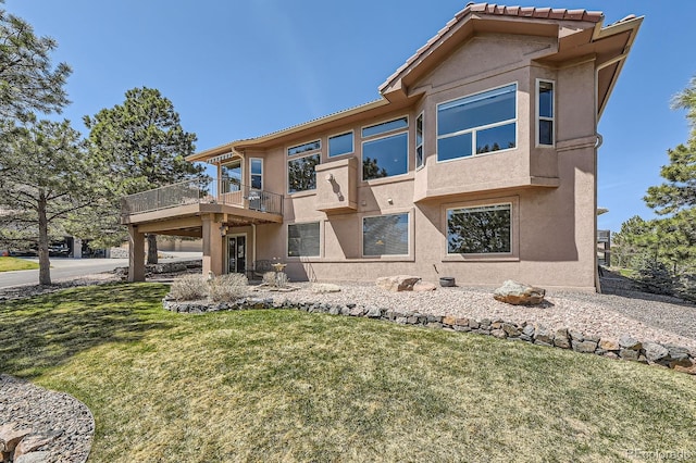 view of front facade with a balcony, a front yard, and stucco siding