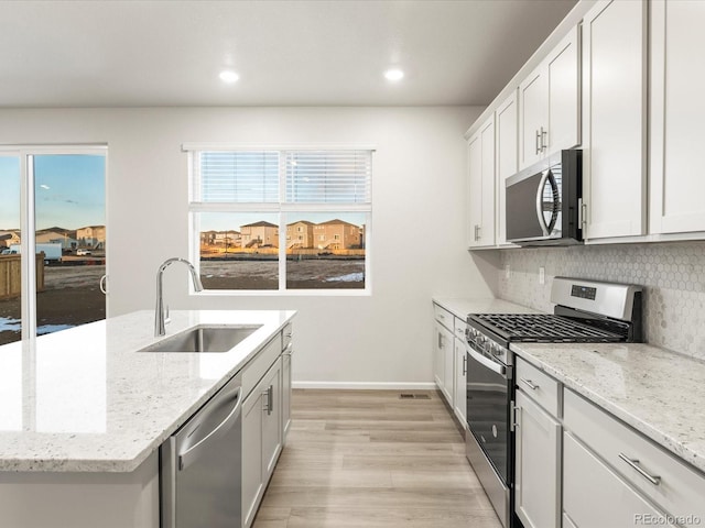 kitchen with sink, appliances with stainless steel finishes, white cabinetry, light stone countertops, and decorative backsplash