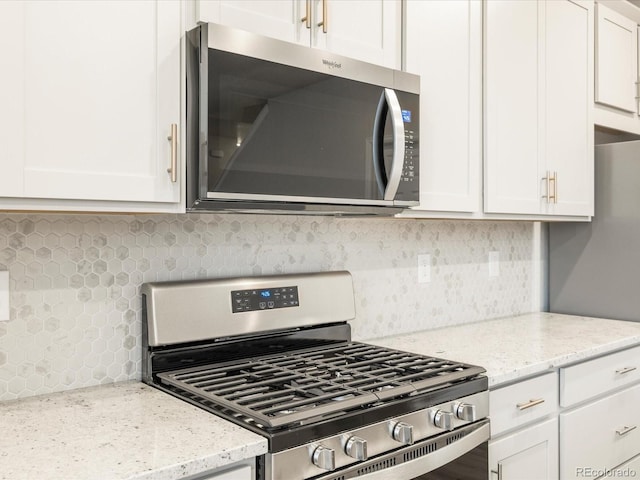 kitchen with white cabinetry, appliances with stainless steel finishes, light stone countertops, and backsplash