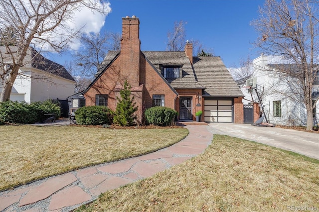 english style home with concrete driveway, brick siding, a chimney, and a front lawn