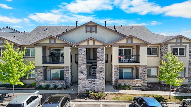 875 E 78th Ave Unit 21, Denver, CO 80229 - view of front facade featuring stucco siding, stone siding, uncovered parking, roof with shingles, and a balcony