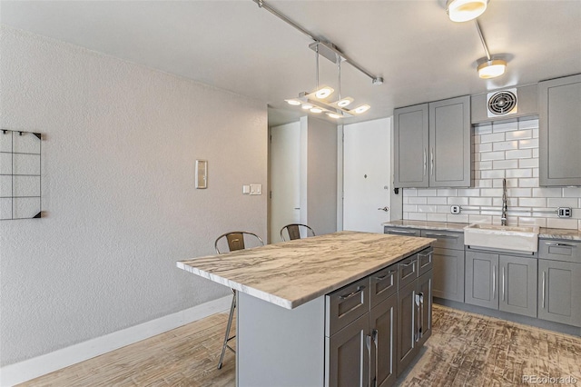 kitchen featuring a kitchen breakfast bar, wood finished floors, a sink, baseboards, and gray cabinetry