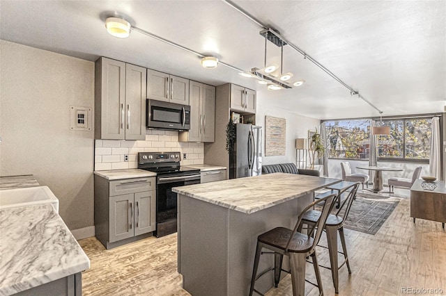 kitchen with appliances with stainless steel finishes, a breakfast bar, light wood finished floors, gray cabinets, and backsplash