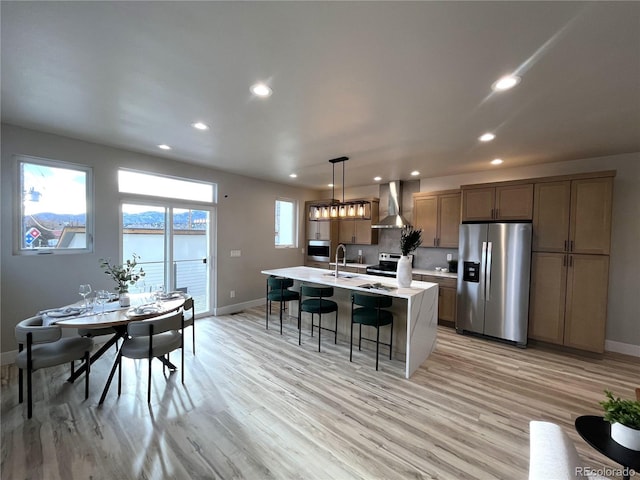 kitchen with a kitchen island with sink, sink, hanging light fixtures, wall chimney exhaust hood, and stainless steel appliances