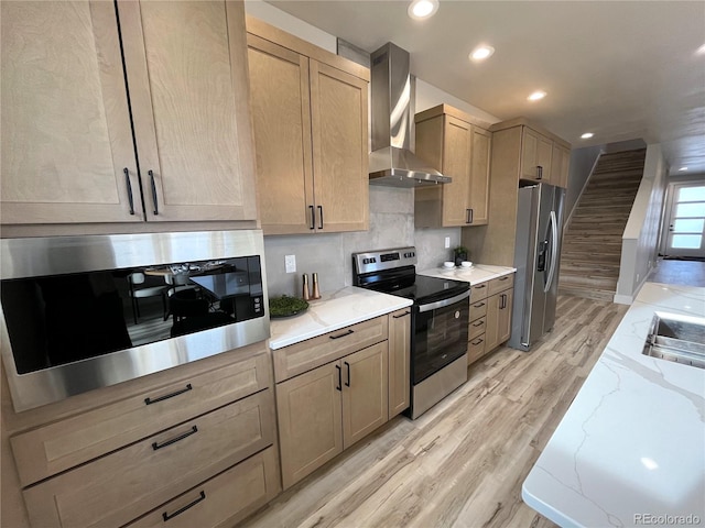 kitchen featuring light wood-type flooring, backsplash, stainless steel appliances, wall chimney range hood, and light brown cabinets