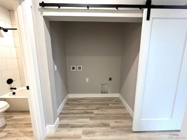 washroom with hookup for an electric dryer, a barn door, light wood-type flooring, and hookup for a washing machine