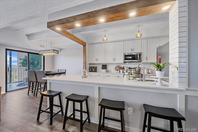 kitchen with wood finished floors, stainless steel appliances, a peninsula, light countertops, and decorative backsplash